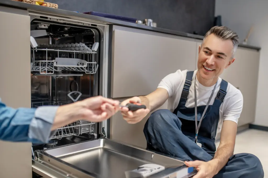 Who Fixes Dishwasher hand holding out tool to plumber sitting on floor