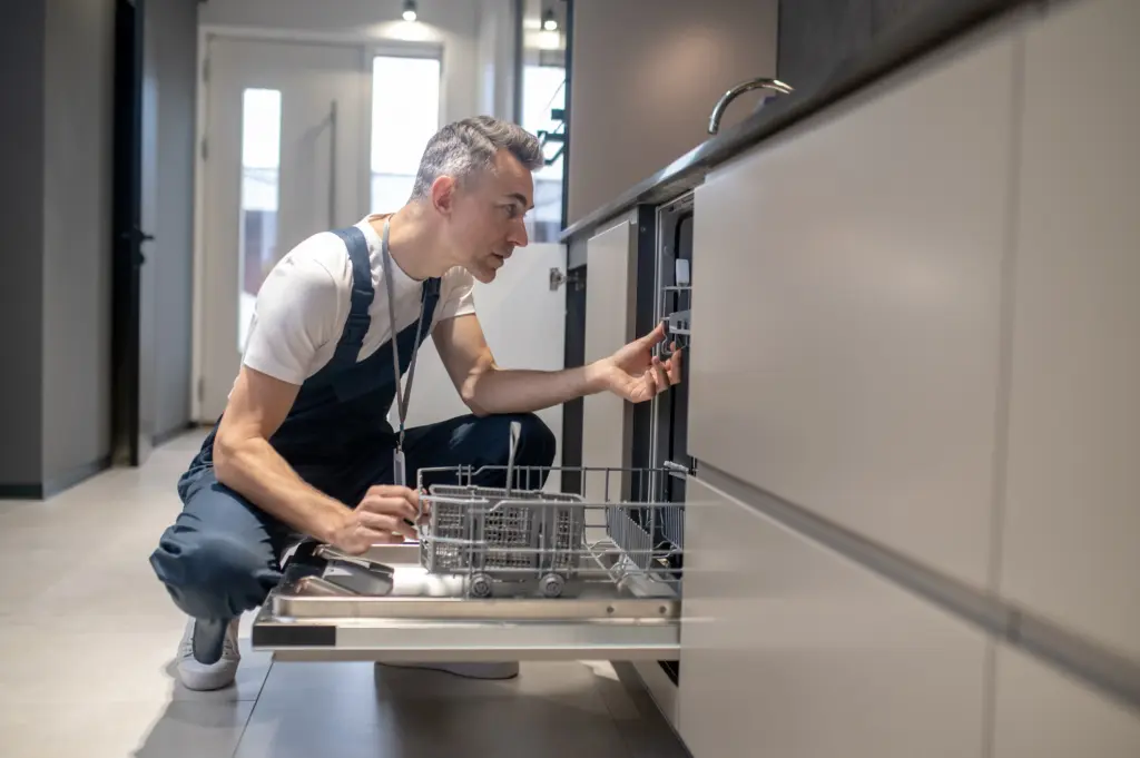 Who Fixes Dishwasher man squatting peeking into dishwasher in kitchen